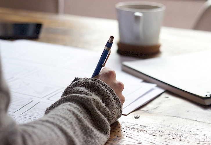 Someone writing, a coffee cup is seen in the distance.